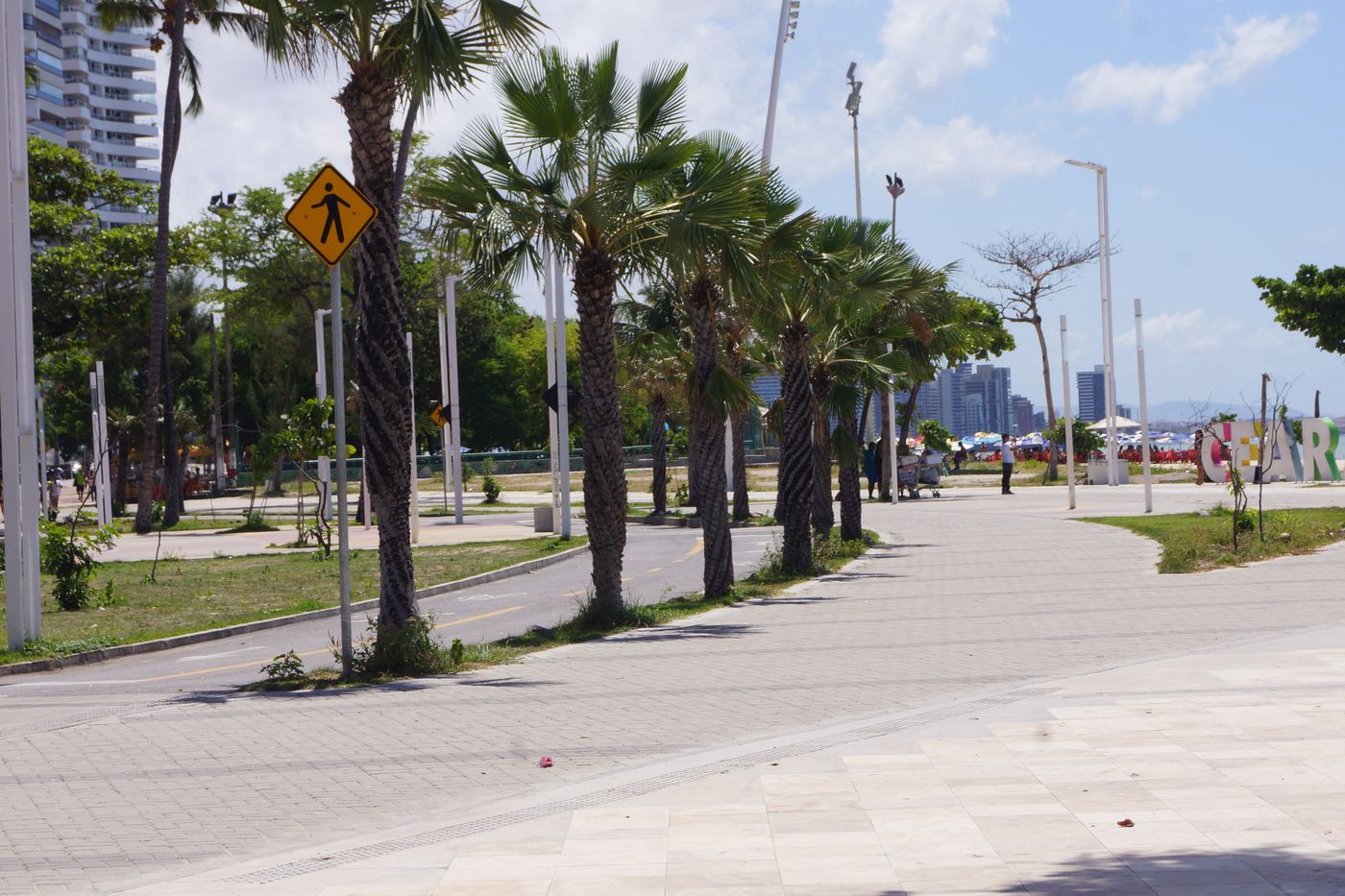 Calçadão da orla de Fortaleza, com coqueiros e o mar ao fundo